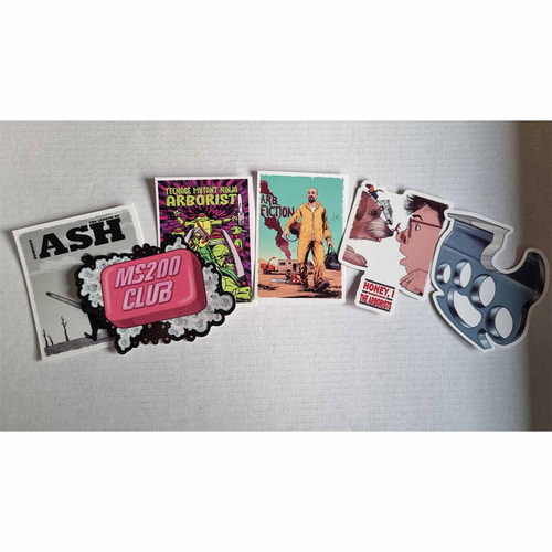 Autocollants ARB Fiction Pack Vol. 5 avec six motifs différents, dont une personne en combinaison jaune, un chien et un humain, une barre de savon rose sur laquelle est écrit « MS200 CLUB », une poignée en métal, un homme avec une tronçonneuse et des pers
