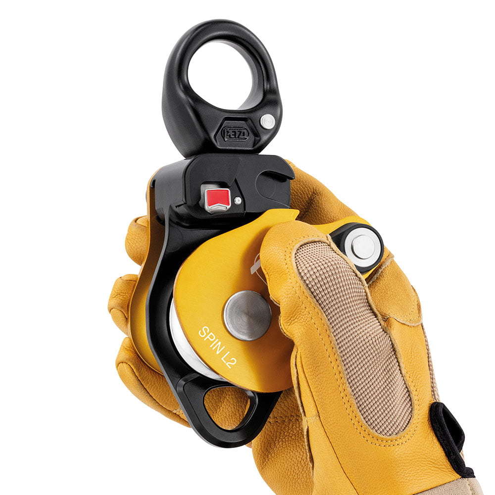 Petzl Spin L2 Block est tenu par une main avec un gant de travail jaune, un boîtier jaune et un mousqueton noir visible