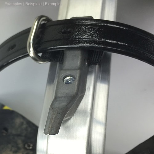 Œillet de guidage en chardon pour le cerclage du cuir attaché à une sangle en cuir noir enroulée autour d’une pièce métallique argentée, visiblement fixée à la partie métallique à l’aide d’une vis