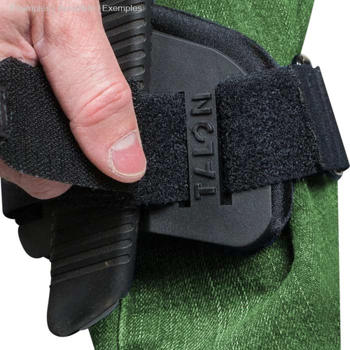 Gros plan d’une main desserrant la sangle velcro de la monture Talon sur un pantalon vert, une scie à main noire est fixée dans le support