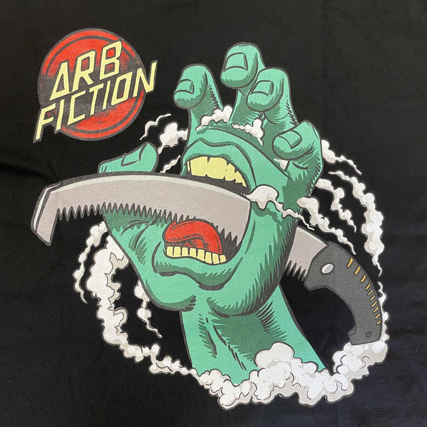 Gros plan de l’impression sur le t-shirt noir avec la main verte, la scie et le logo rouge « ARB FICTION », nom du produit Screaming Hand