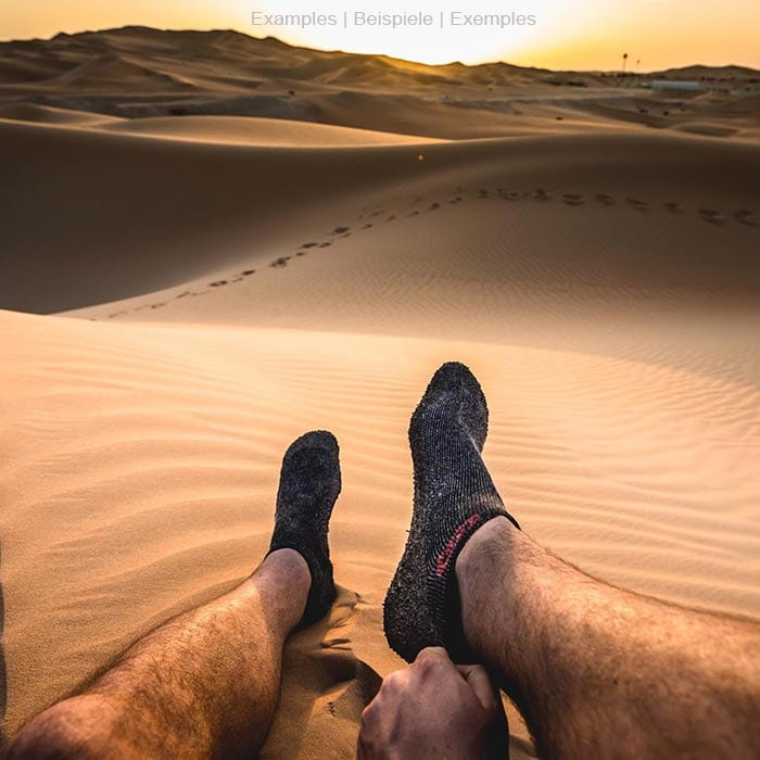 Chaussette noire de Skinner avec semelle caoutchoutée sur un pied dans le désert, en arrière-plan dunes de sable au coucher du soleil