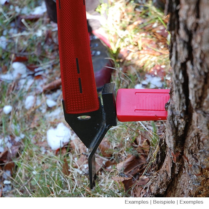 Cric d’abattage 600 de Stubai en cours d’utilisation, poignée rouge et pointe en métal noir sur un tronc d’arbre, broyé avec de l’herbe et des feuilles visibles