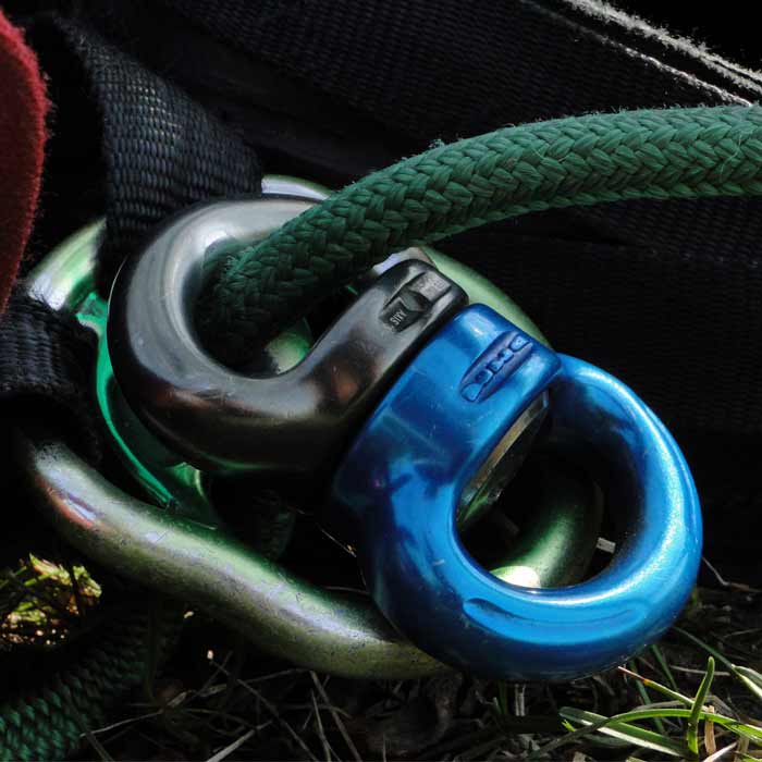 Axe Swivel S, point de connexion pivotant en bleu et noir relié à une corde verte et à d’autres accessoires métalliques sur le sol en herbe