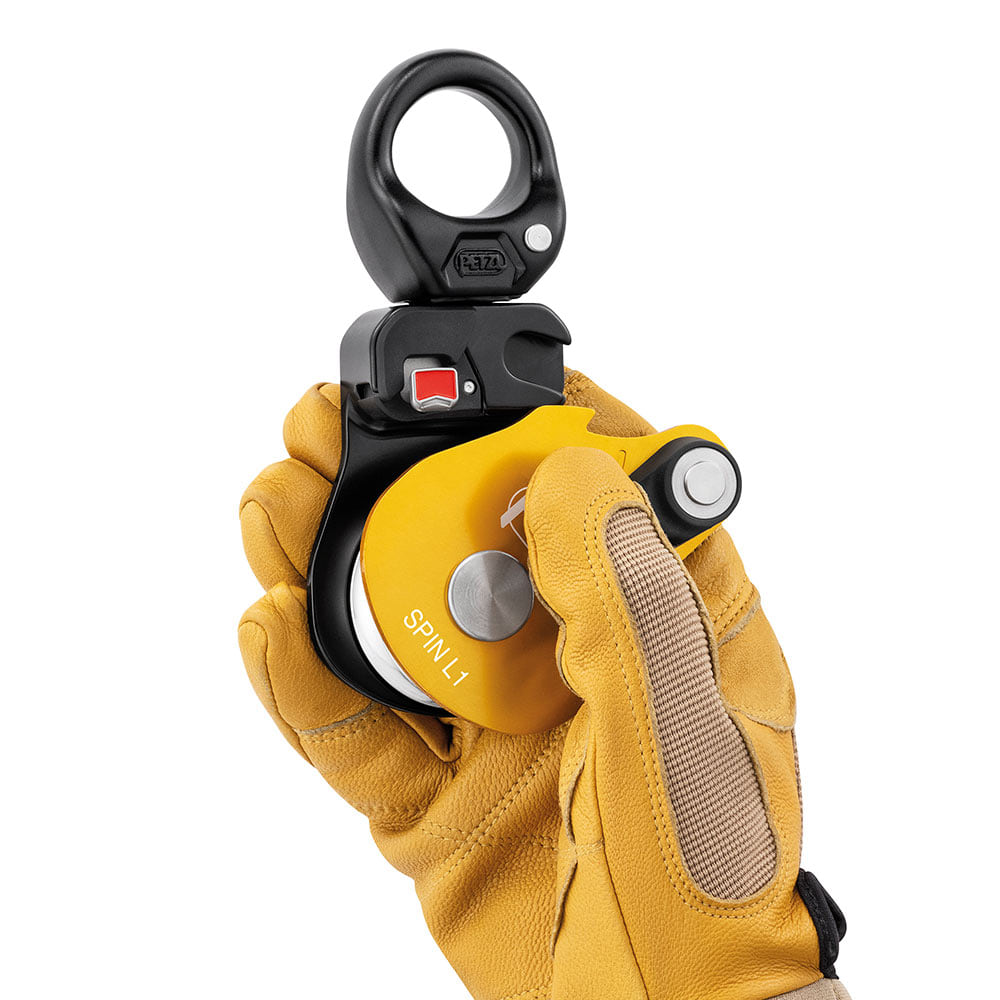 Poulie à corde Petzl Spin L1 avec boîtier jaune, tenue d’une main avec gant de travail jaune