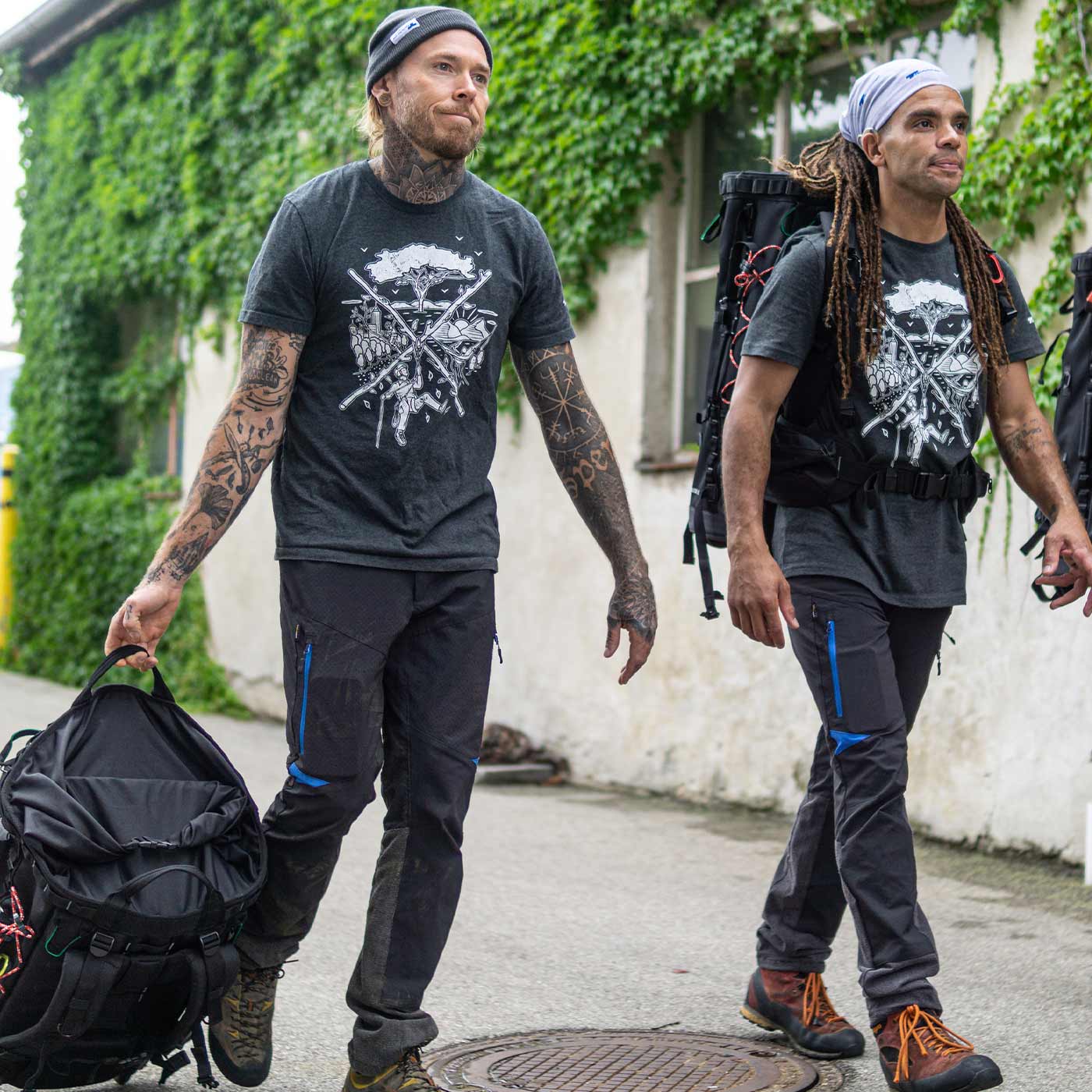 Deux hommes portent le t-shirt tSPIRIT gris foncé avec un motif blanc d’escalade et de nature, l’un porte une casquette noire et tient un sac, l’autre porte un foulard de couleur claire et un sac à dos
