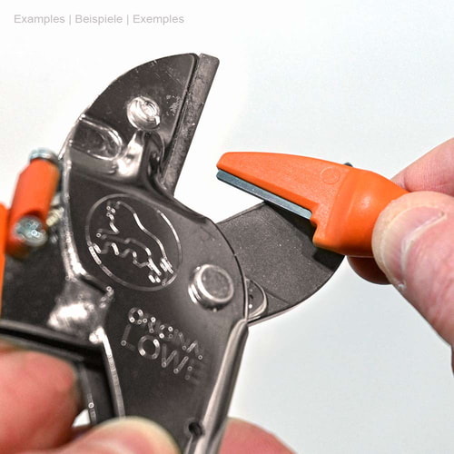 La main tient l’aiguiseur de lame orange Original LÖWE et l’utilise pour affûter un sécateur noir avec le logo LÖWE
