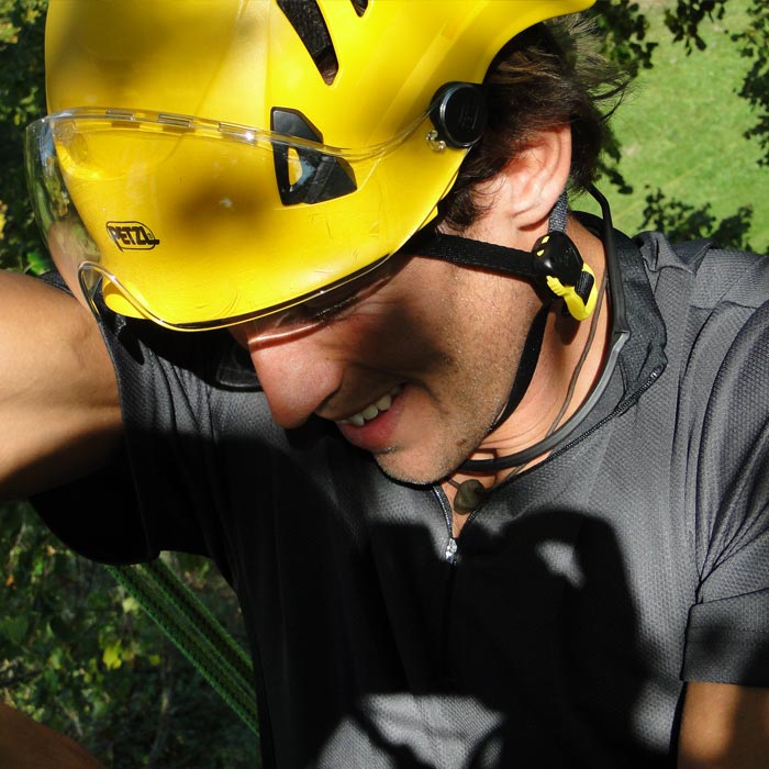 Homme avec un casque Petzl jaune portant un bouclier de protection Vizir transparent sur son casque, il porte un T-shirt gris et est à l’extérieur