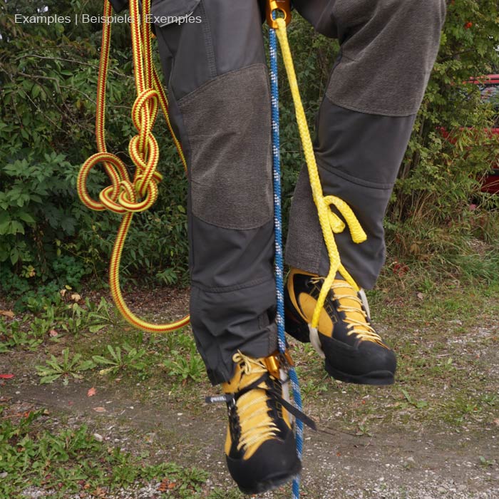 Outil élastique bleu avec section élastique et ondulée et sangle plate avec bordure noire et bande intérieure verte sur un pantalon d’extérieur gris avec des chaussures d’alpinisme jaunes et noires et plusieurs cordes d’escalade