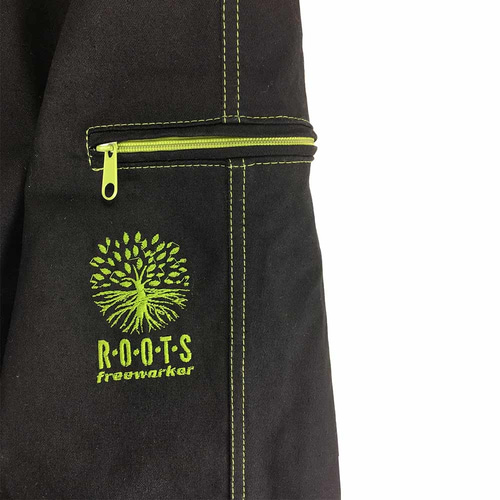 Gros plan d’une poche du pantalon d’extérieur Roots Pure en noir avec fermeture éclair verte et coutures vertes, broderie verte d’un arbre avec inscription « ROOTS freeworker »