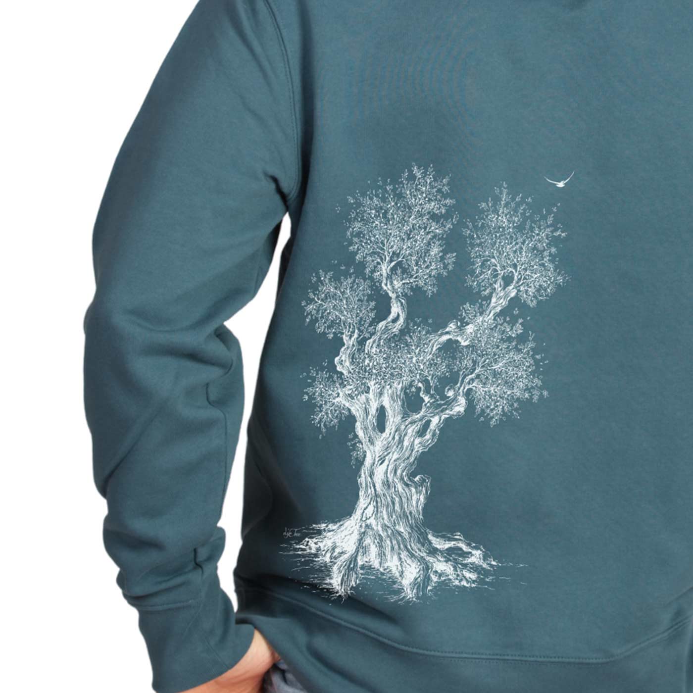 Sweat à capuche Olive Tree en sarcelle, détail de l’imprimé arbre blanc au dos, porté par une personne ayant la main dans la poche de son pantalon