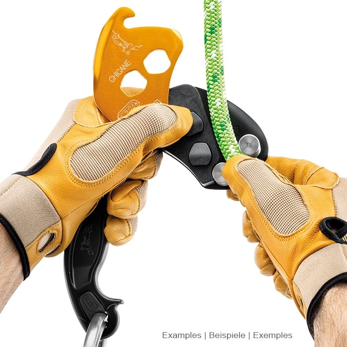 Chicane Petzl, appareil d’assurage jaune et noir avec poignée, tenu par deux mains avec des gants jaunes sur une corde verte