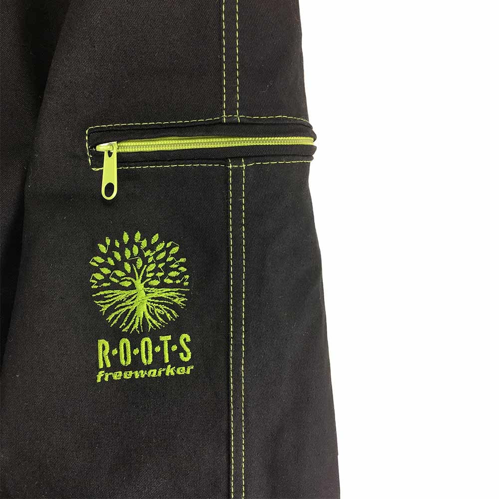 Gros plan d’une poche du pantalon d’extérieur Roots Pure en noir avec fermeture éclair verte et coutures vertes, broderie verte d’un arbre avec inscription « ROOTS freeworker »
