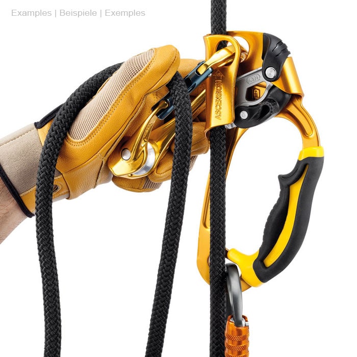 Un mousqueton orange sur corde noire, tenu par une main avec un gant jaune, relié à un dispositif d’escalade jaune et noir et à un mousqueton orange au bas