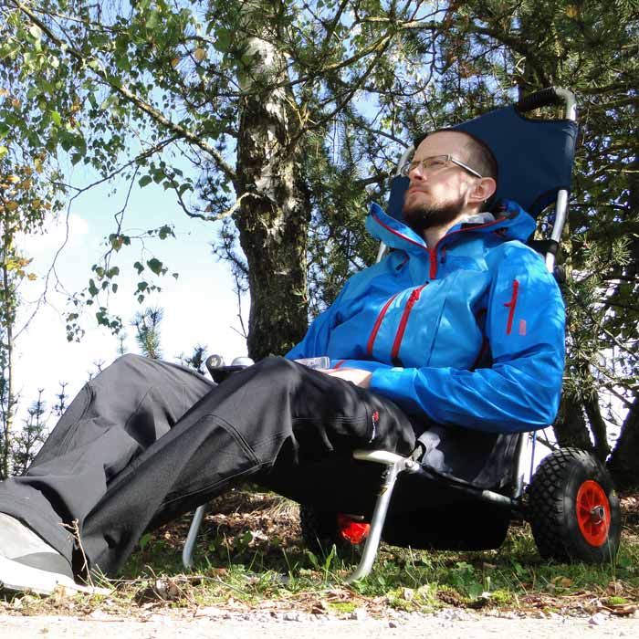 Homme assis dans un fauteuil roulant de plage bleu foncé à l’extérieur entouré d’arbres