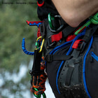 skyHOOK Open Gate en bleu et rouge attaché à un harnais d’escalade, utilisé par une personne avec du matériel d’escalade