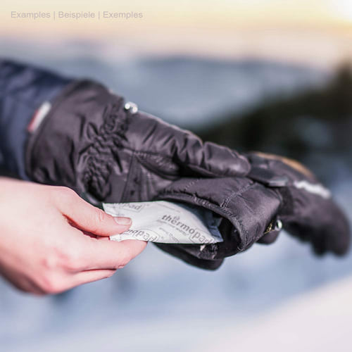 Le chauffe-mains du thermopad est tenu dans la main par une personne en gant d’hiver noir à moitié, le coussin chauffant est imprimé en blanc avec le lettrage thermopad noir