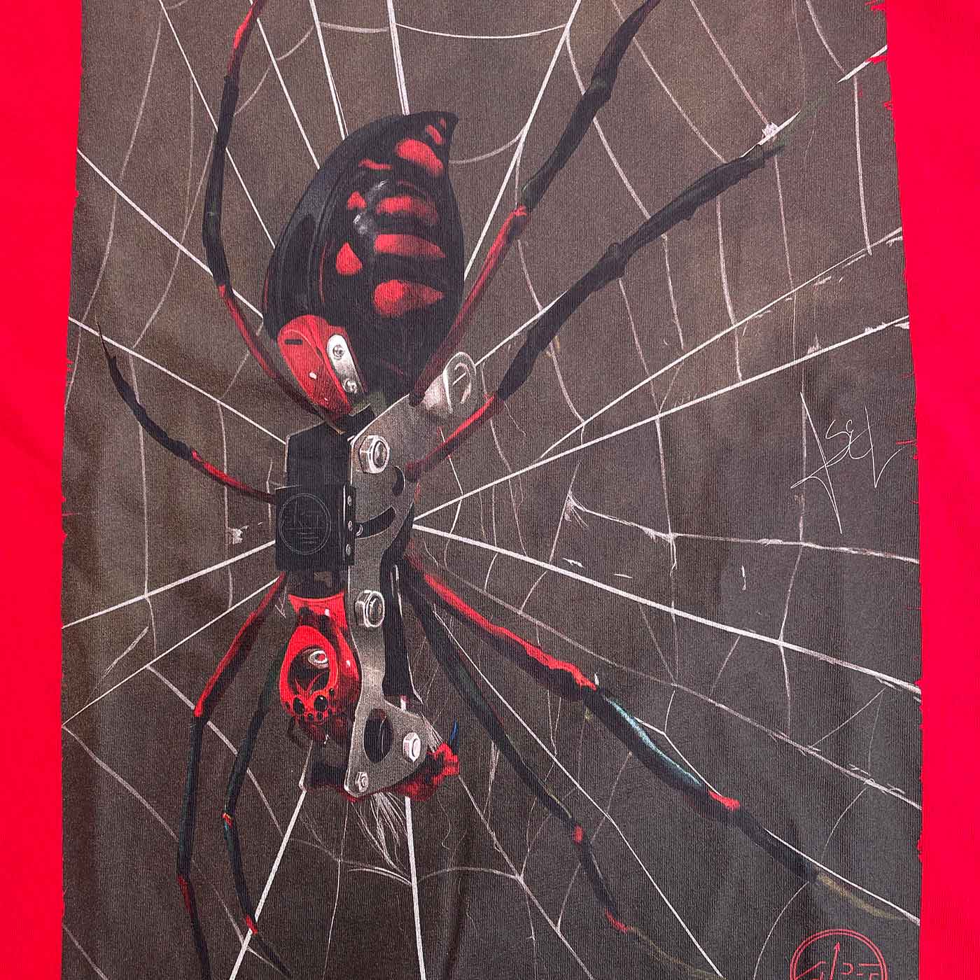 Gros plan de l’imprimé araignée sur la chemise rouge ART Spider, l’araignée a des couleurs noires et rouges et se trouve sur une toile d’araignée blanche sur un fond sombre