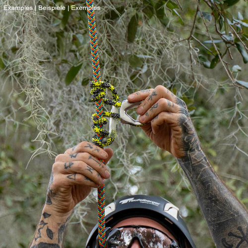 prusikLOOP fimble, une corde d’escalade avec une partie en métal argenté, tenue par les mains tatouées d’une personne avec un casque, dans un environnement forestier