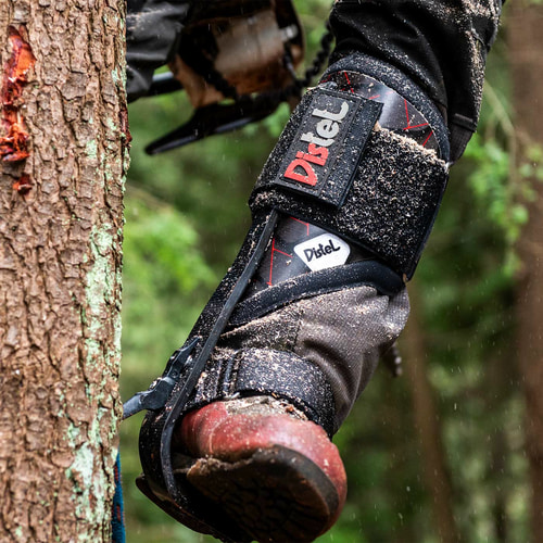 Distel Carbon 3.1 Velcro de Distel, éperon de via ferrata sur la jambe d’un porteur touchant un tronc d’arbre, avec saleté visible sur l’éperon et la chaussure