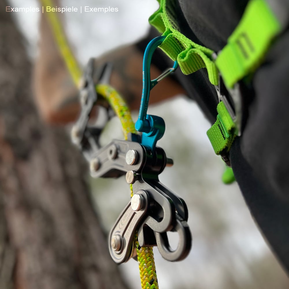 Personne portant un harnais vert avec un mousqueton Magneato bleu attaché à celui-ci, relié à un cadre d’escalade noir et à une corde jaune, à l’extérieur sur un arbre.