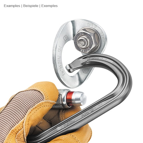 Coeur Stainless 12 de Petzl, pièce en métal argenté avec mousqueton, tenue d’une main par un gant de travail jaune et mousqueton noir avec mécanisme de verrouillage rouge