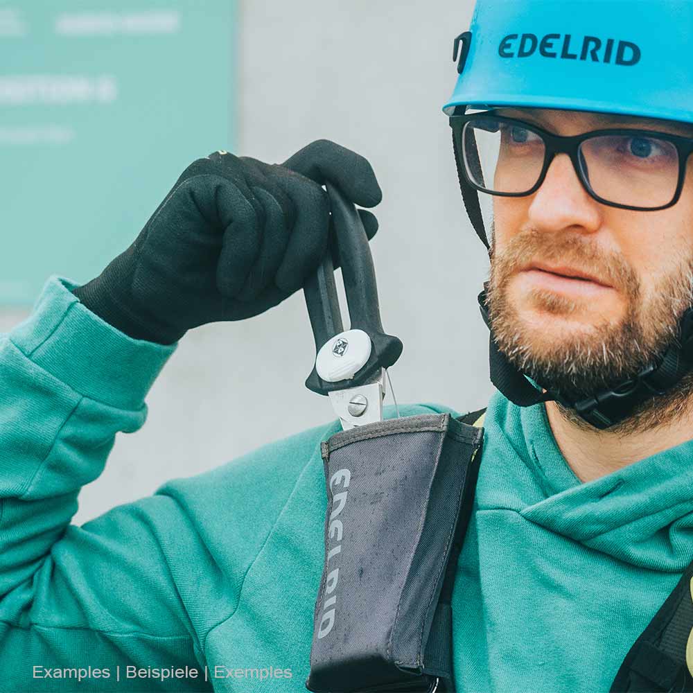Homme en casque de sécurité Edelrid bleu et veste verte tenant des ciseaux noirs de l’étui de sauvetage Edelrid noir d’Edelrid