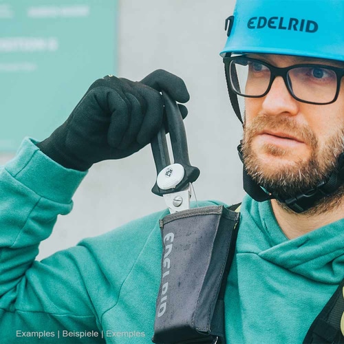 Homme en casque de sécurité Edelrid bleu et veste verte tenant des ciseaux noirs de l’étui de sauvetage Edelrid noir d’Edelrid
